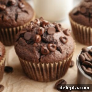 Decadent Double Chocolate Espresso Muffins 10 A close up of a double chocolate espresso muffin on brown parchment paper, showcasing its perfect dome and chocolate chips.