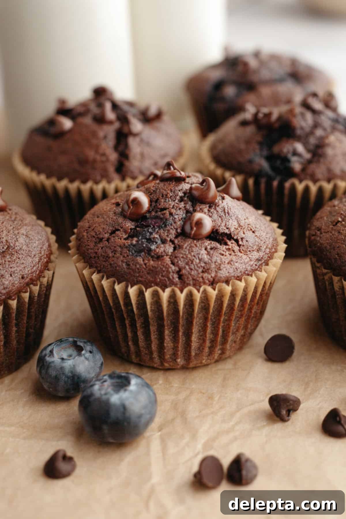 Decadent Blueberry Chocolate Sour Cream Muffins 2 A perfectly baked, extra moist blueberry chocolate muffin, speckled with blueberries and chocolate chips, resting on parchment paper, ready to be enjoyed.