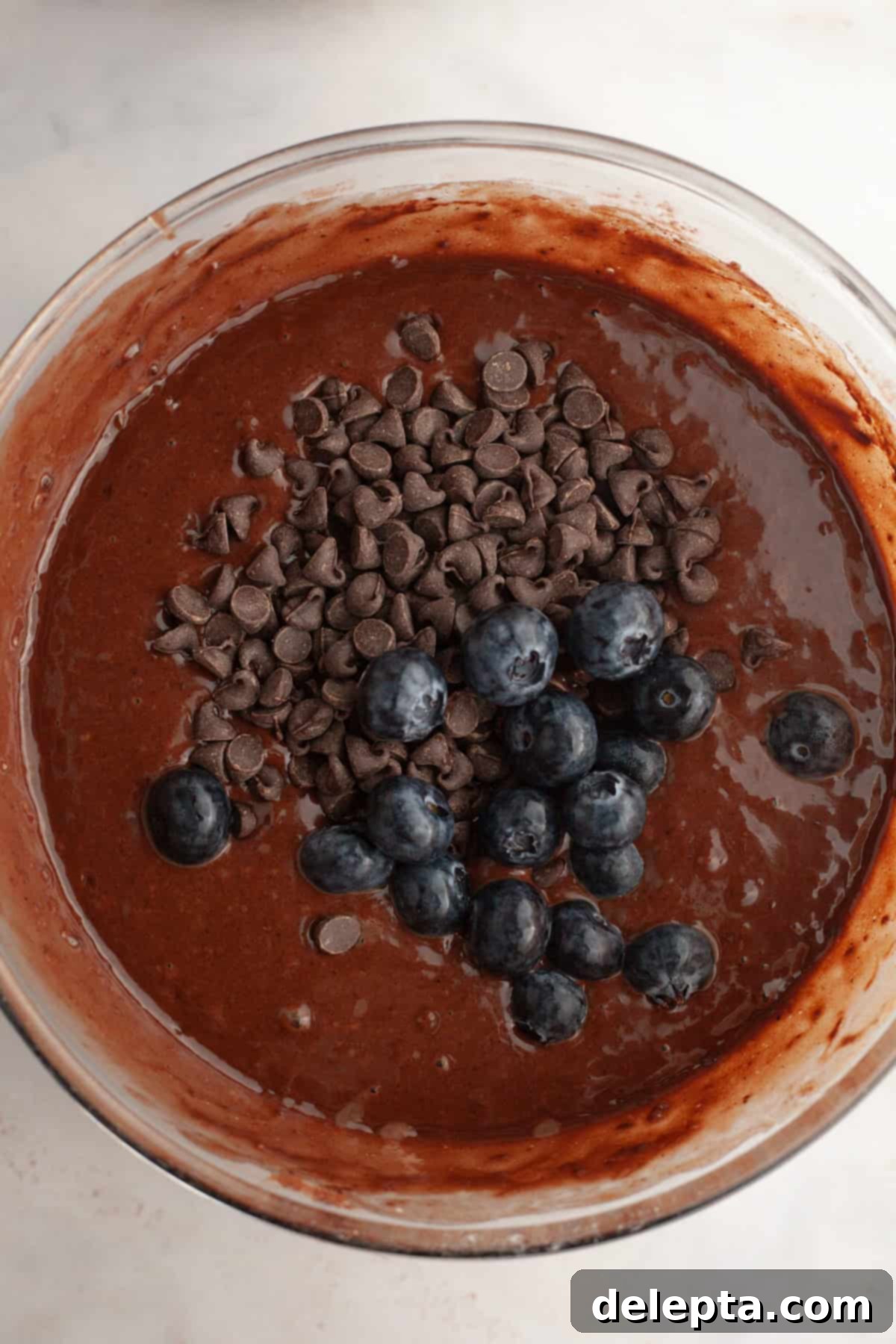 Decadent Blueberry Chocolate Sour Cream Muffins 6 Chocolate muffin batter in a glass bowl, with semisweet chocolate chips and fresh blueberries gently folded in, showcasing the vibrant ingredients.