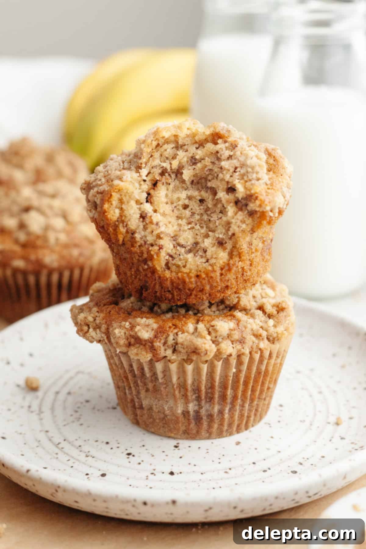 Cinnamon Crumble Banana Muffins 2 A stack of two perfectly baked banana coffee cake muffins, one with a delightful bite taken out, revealing the moist interior and cinnamon swirl.