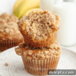 Cinnamon Crumble Banana Muffins 12 A stack of two banana coffee cake muffins, one has a bite taken out of it.