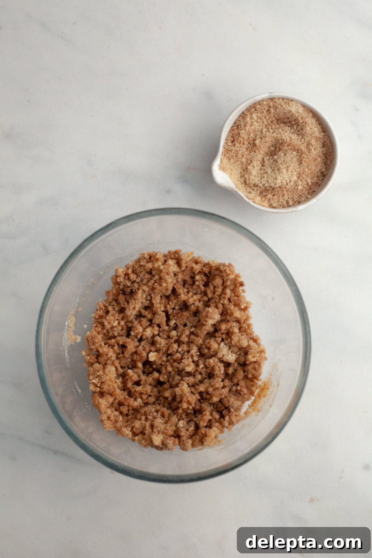 Cinnamon Crumble Banana Muffins 7 Freshly prepared streusel topping in a clear glass bowl, alongside a small bowl of cinnamon sugar for the swirl.
