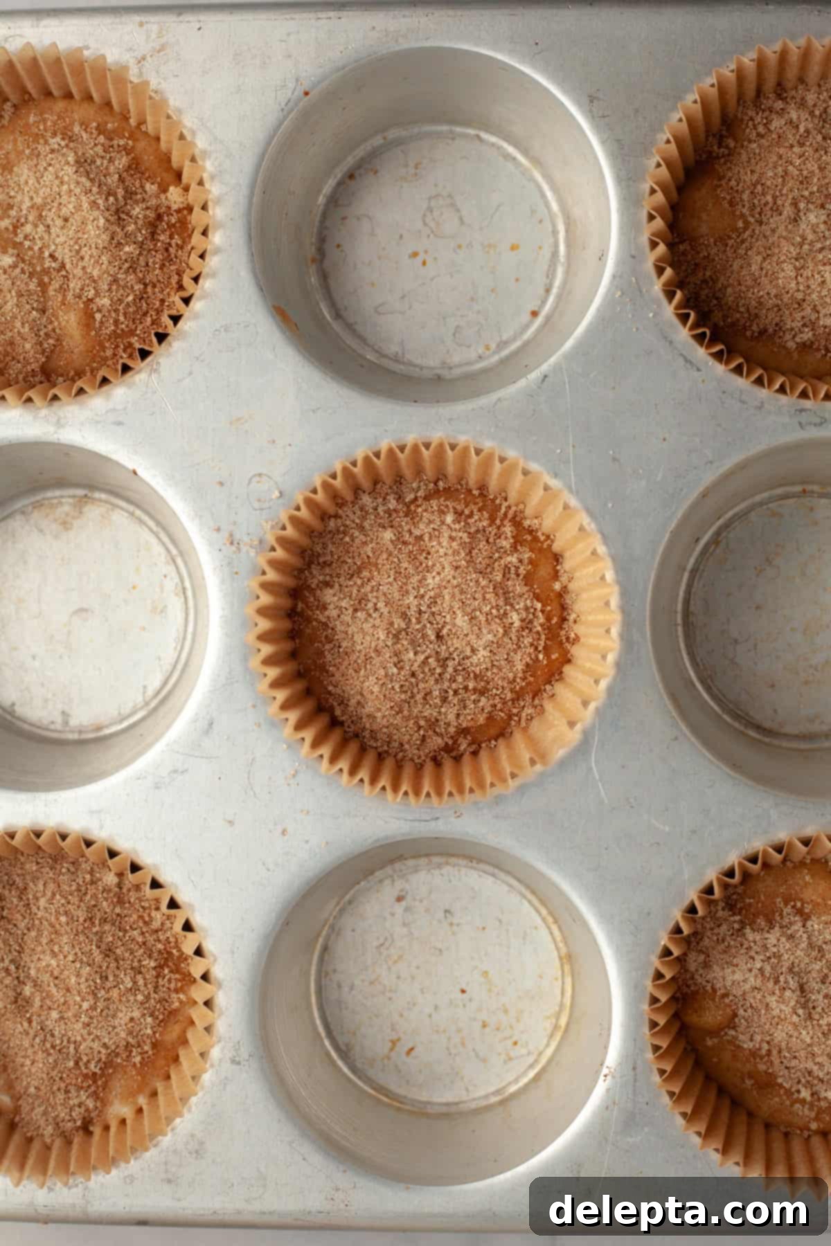 Cinnamon Crumble Banana Muffins 8 A muffin pan filled with unbaked banana muffins, layered with cinnamon sugar, ready for the next step of baking.