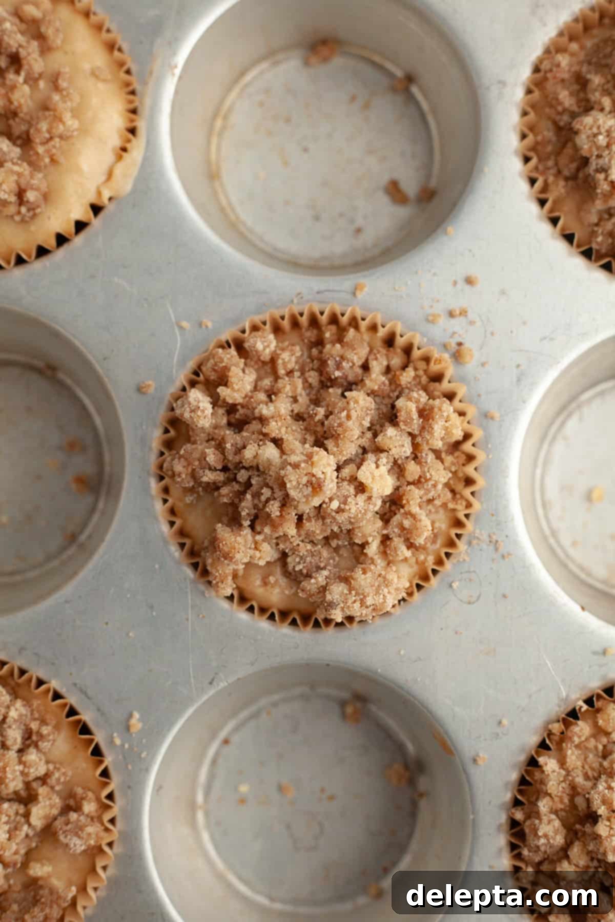 Cinnamon Crumble Banana Muffins 9 An unbaked muffin pan showcasing banana muffins generously topped with crumbly streusel, ready for baking.