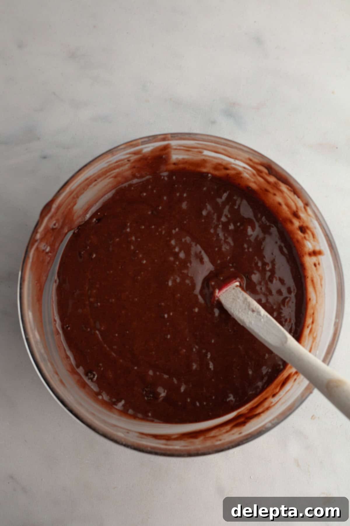 Decadent Double Chocolate Strawberry Muffins 5 A glass bowl with chocolate muffin batter in it and a rubber spatula, showing the mixture after dry ingredients are added.
