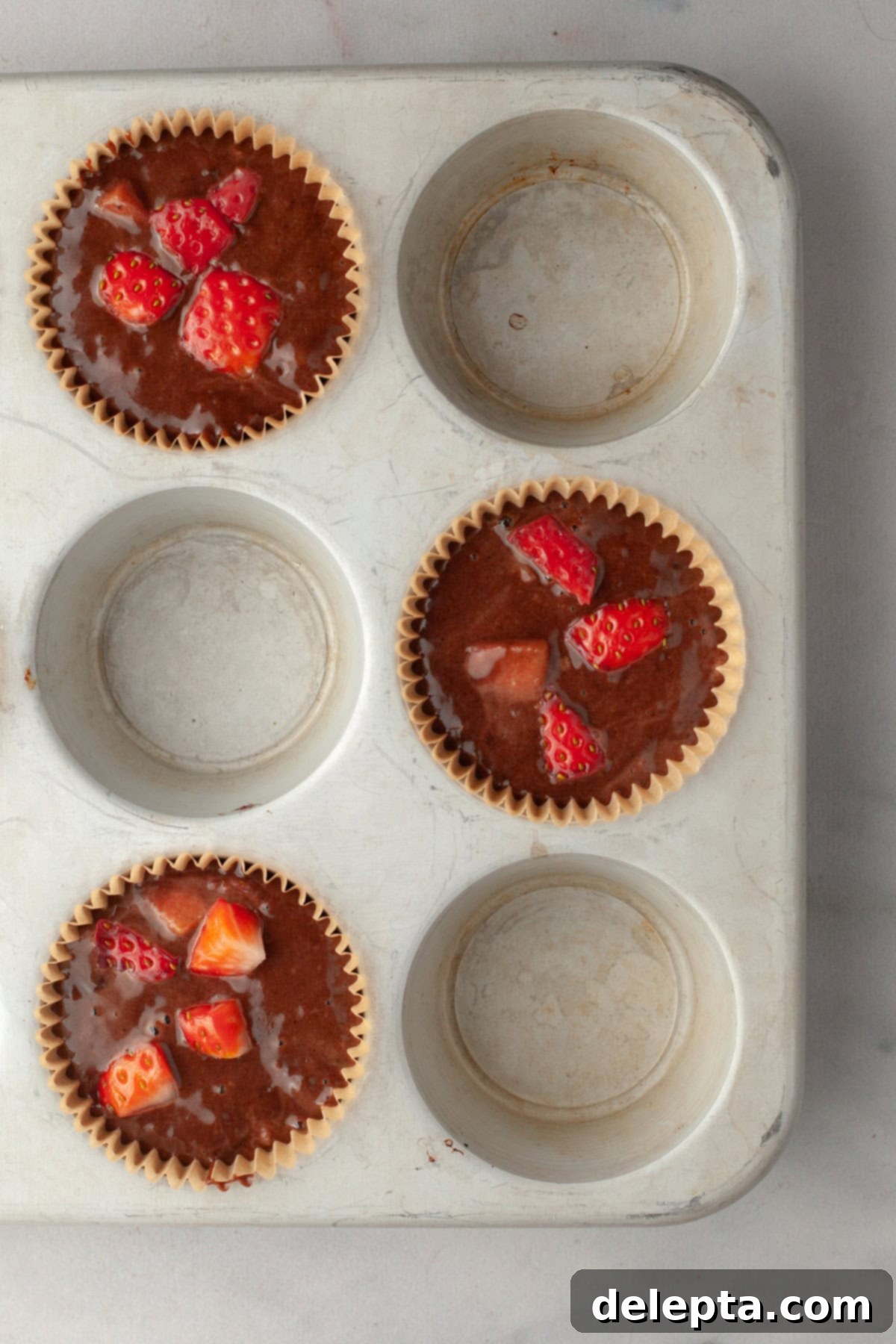 Decadent Double Chocolate Strawberry Muffins 7 Unbaked chocolate strawberry muffins in a muffin pan, filled and ready for the oven.