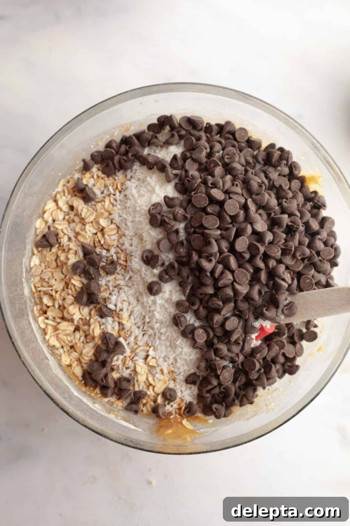 Brown Butter Oatmeal Cookies with Chocolate Chips and Coconut 7 A glass bowl with cookie dough, showing rolled oats, chocolate chips, and shredded coconut folded in.