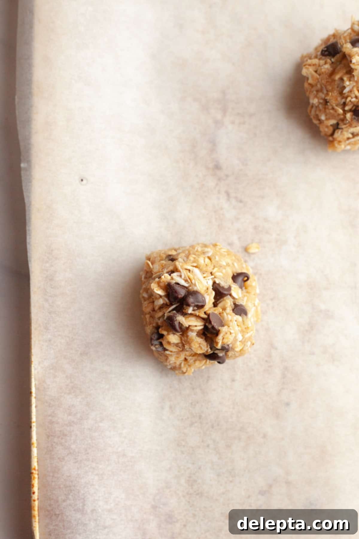 Brown Butter Oatmeal Cookies with Chocolate Chips and Coconut 8 An unbaked oatmeal coconut chocolate chip cookie dough ball, perfectly portioned, on parchment paper.
