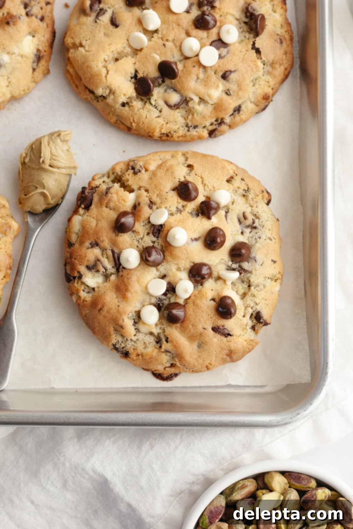 Pistachio Stuffed Chocolate Chip Delights 9 Large pistachio and chocolate chip cookies baking on a parchment-lined baking sheet, golden and perfectly puffed, with melted chocolate visible.