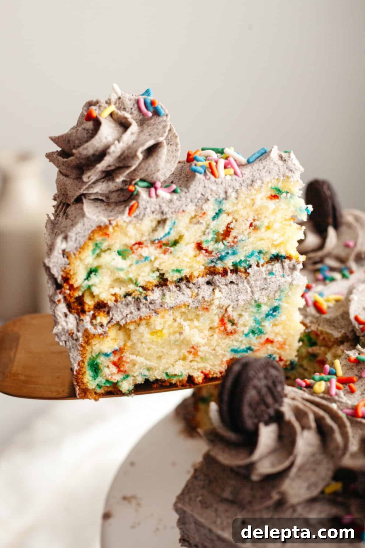 Simply Delicious Funfetti Oreo Cake with Dreamy Oreo Frosting 11 A slice of Funfetti Oreo cake being lifted from the cake with a cake server, revealing its moist layers and rich frosting.