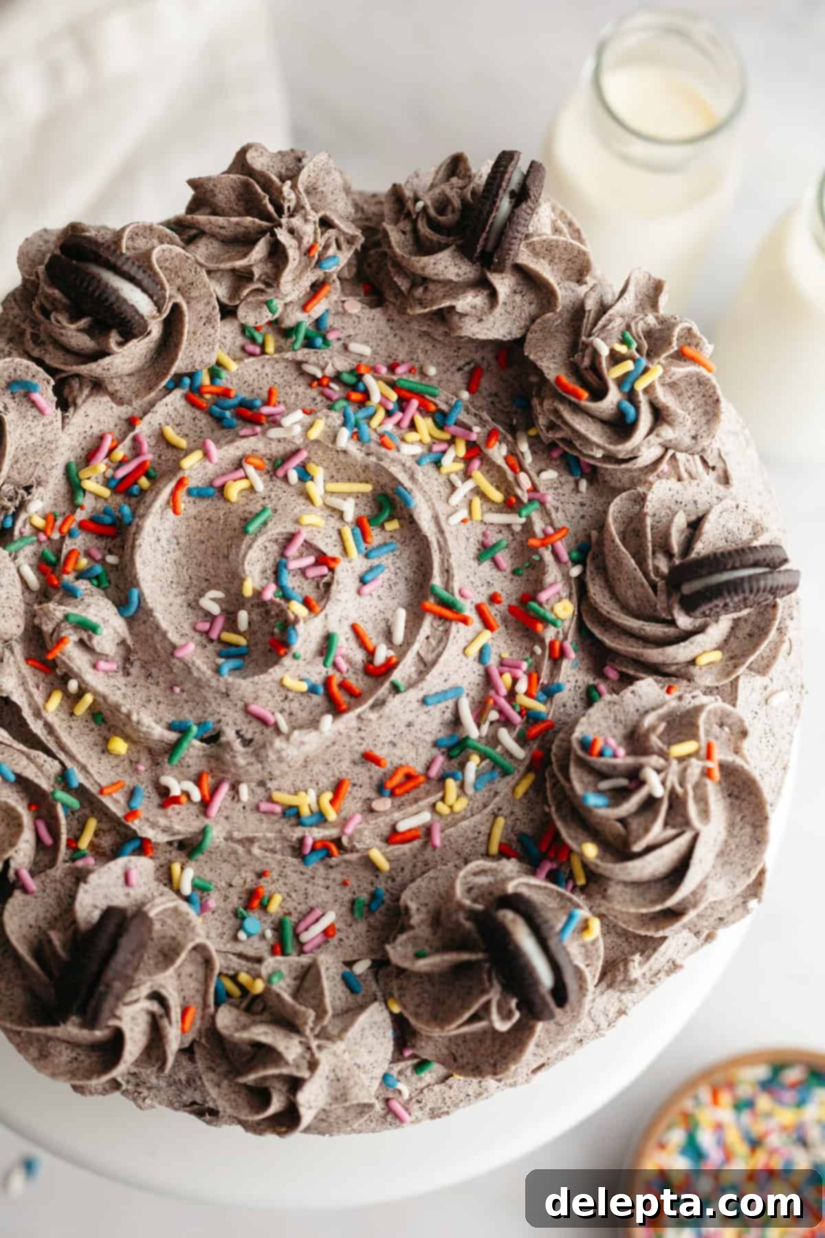 Simply Delicious Funfetti Oreo Cake with Dreamy Oreo Frosting 10 An overhead shot of a decorated Oreo frosted cake with a swirl on top, garnished with rainbow sprinkles and mini Oreos.