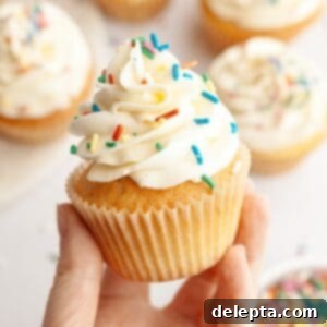 Pure Vanilla Bean Bliss Cupcakes 11 A hand holding a vanilla bean cupcake with rainbow sprinkles.