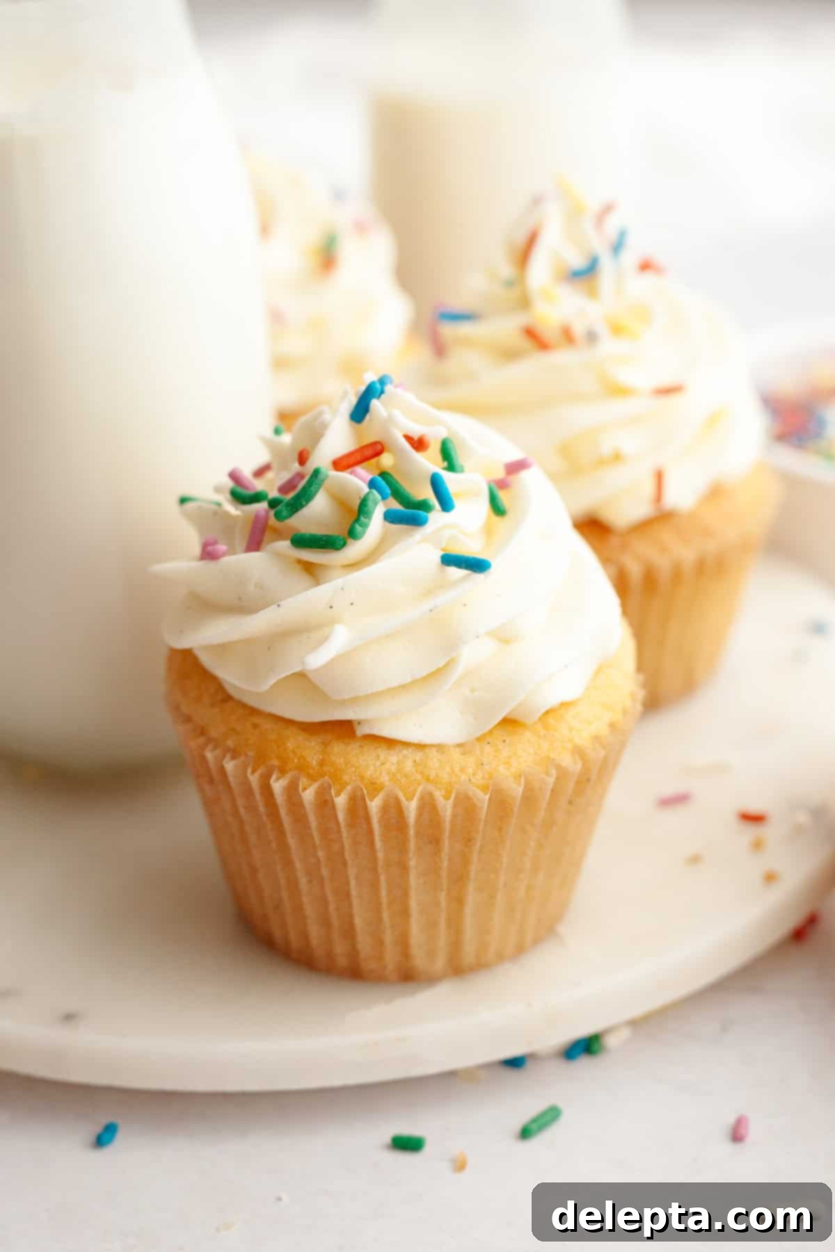 Pure Vanilla Bean Bliss Cupcakes 10 A close up of a single, elegantly frosted vanilla bean cupcake, generously topped with an assortment of colorful rainbow sprinkles.