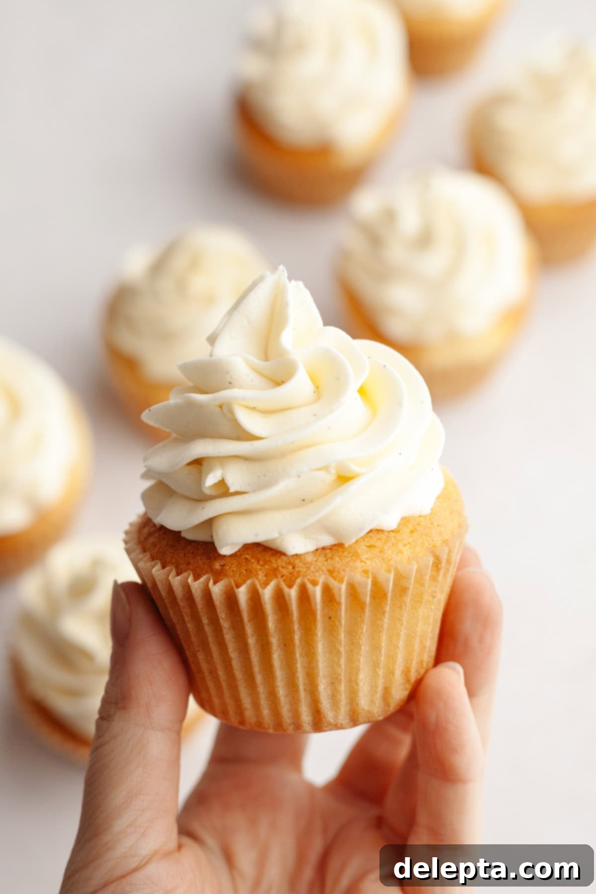 Simple Vanilla Bean Buttercream Perfection 2 A hand holding a vanilla cupcake with vanilla bean buttercream.