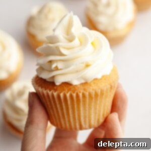 Simple Vanilla Bean Buttercream Perfection 7 A hand holding a cupcake with vanilla bean buttercream.