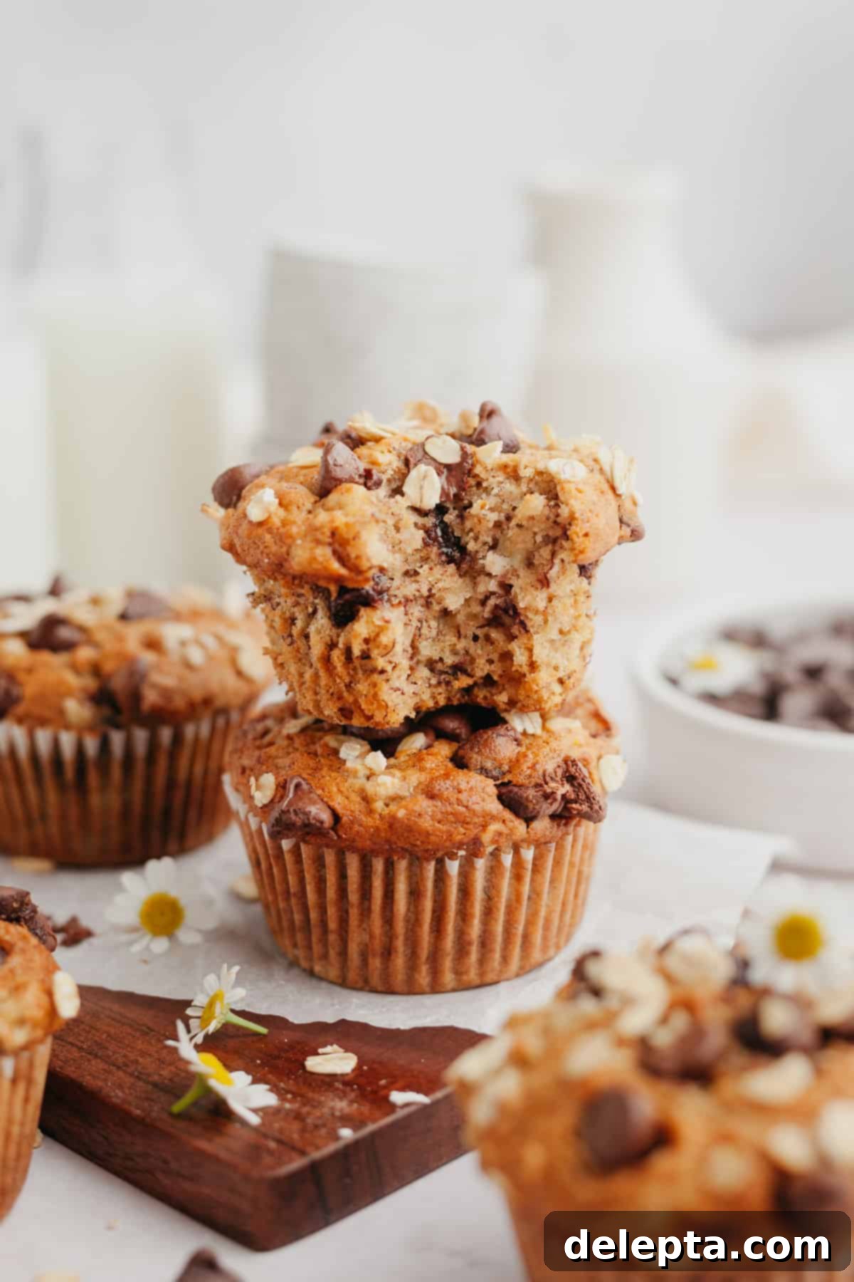 Wholesome Banana Oat Chocolate Chip Muffins 2 Two stacked oatmeal banana chocolate chip muffins, the top muffin has a bite taken out of it, revealing its soft, fluffy texture and chocolate chips.