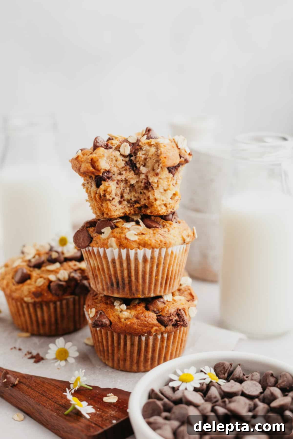 Wholesome Banana Oat Chocolate Chip Muffins 7 Three stacked oatmeal banana chocolate chip muffins on a cutting board, the top one with a bite taken out, showing its moist interior.