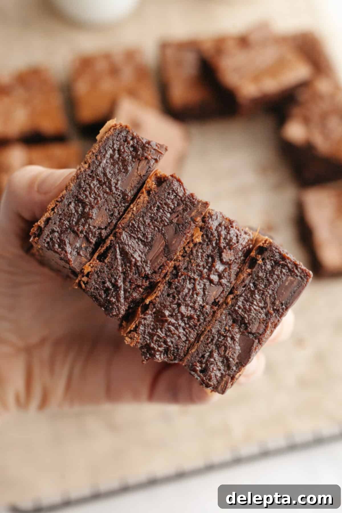 Decadent One Bowl Fudgy Brown Butter Espresso Brownies 10 A hand holding a stack of four fudgy brown butter espresso brownies, emphasizing their rich appearance.
