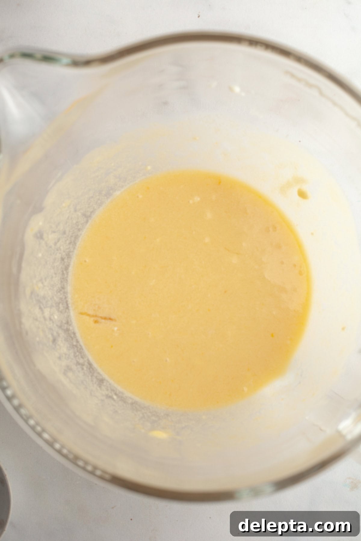 Raspberry Almond Jam Burst Cupcakes 5 A glass bowl containing a yellow liquid mixture, indicating the wet ingredients for the cupcake batter.