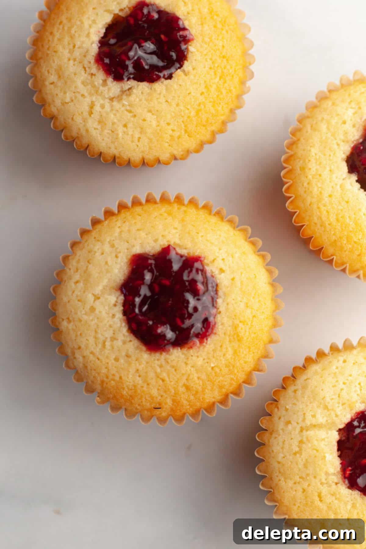 Raspberry Almond Jam Burst Cupcakes 9 Almond cupcakes cored and generously filled with bright red raspberry jam, ready for frosting.