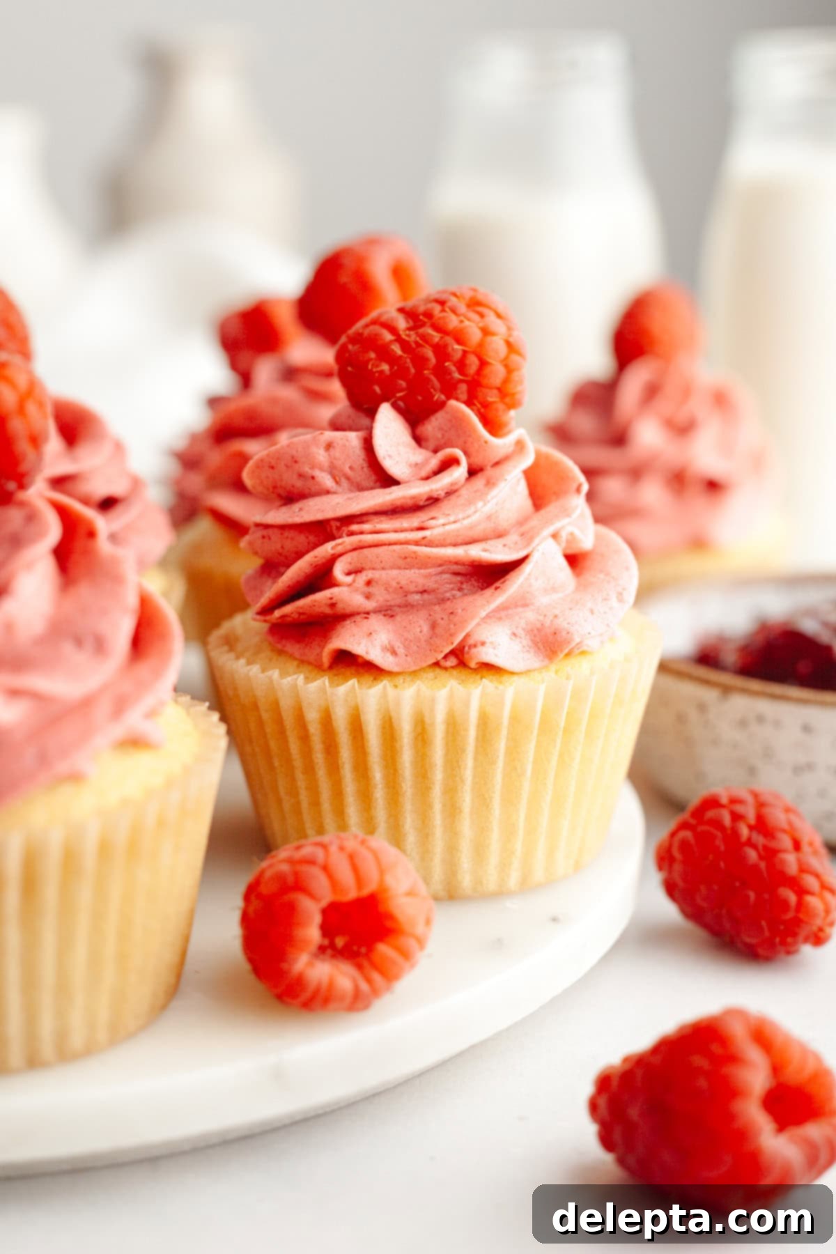 Raspberry Almond Jam Burst Cupcakes 10 Beautifully frosted raspberry almond cupcakes topped with fresh raspberries, arranged elegantly on a serving platter.