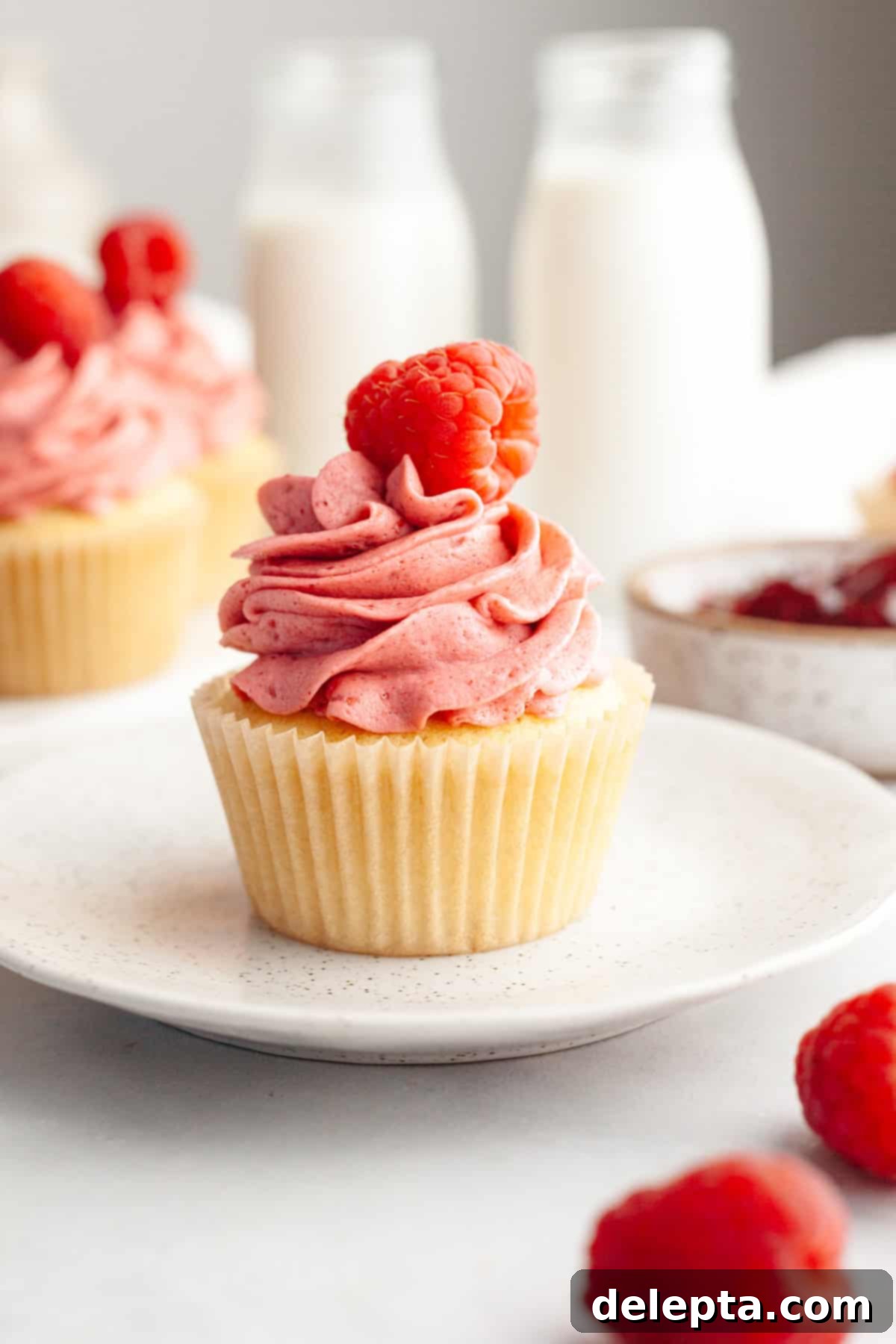 Raspberry Dream Buttercream 6 A beautifully frosted raspberry almond cupcake on a small white plate, ready to be enjoyed.