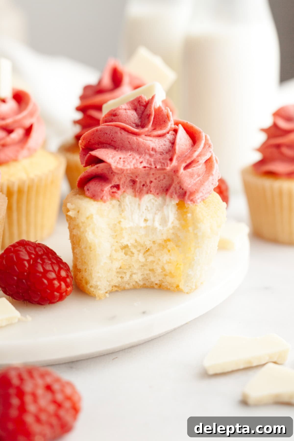 Decadent Raspberry White Chocolate Ganache Cupcakes 2 A vanilla cupcake with a bite taken out of it, it has a white chocolate ganache filling and pink frosting.