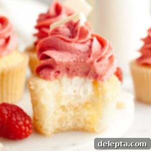 Decadent Raspberry White Chocolate Ganache Cupcakes 14 A vanilla cupcake with a bite taken out of it, it has a white chocolate ganache filling and pink frosting.
