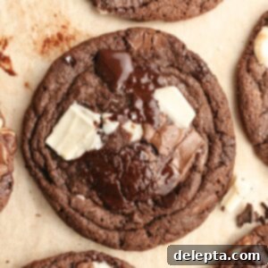 Chewy Triple Chocolate Chunk One Bowl Cookies 10 A close up of a triple chocolate chunk cookie on brown parchment paper, showing its chewy texture and chocolate puddles.