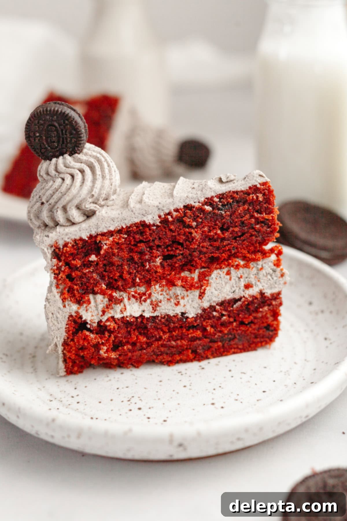 Red Velvet Oreo Cake with Oreo Buttercream 12 A delicious slice of red velvet cake with creamy Oreo frosting on a small white plate, ready to be enjoyed.