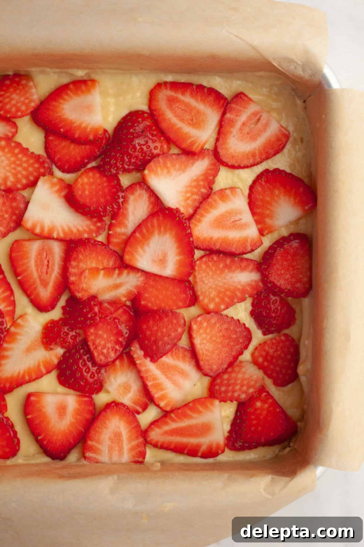 Simple One-Bowl Strawberry Snack Cake 6 Unbaked cake in a square pan covered with sliced strawberries.