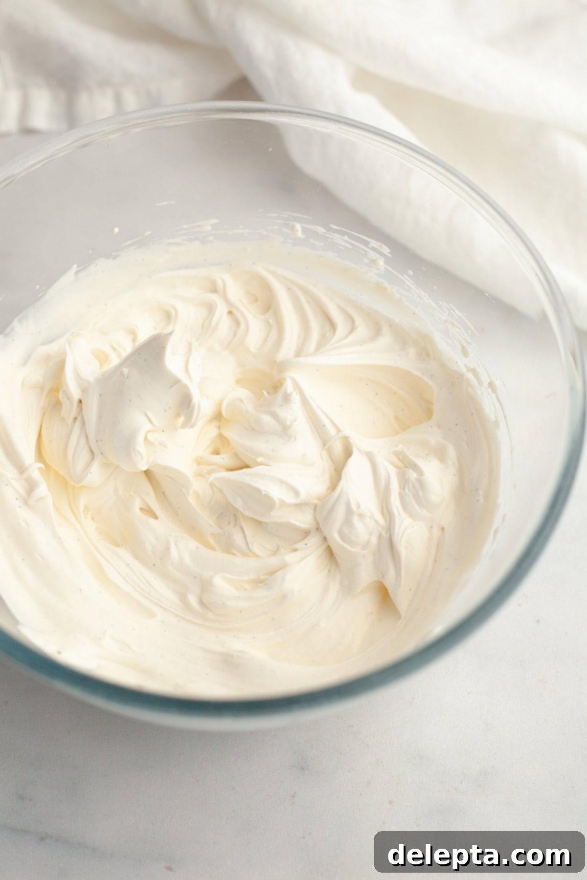 Simple Homemade Vanilla Bean Whipped Cream 2 A glass bowl with homemade vanilla bean whipped cream, showing visible vanilla bean flecks.