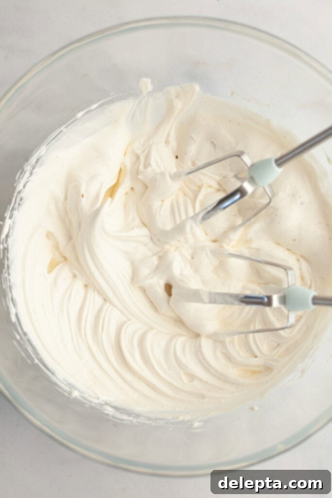 Simple Homemade Vanilla Bean Whipped Cream 4 A glass bowl with vanilla bean whipped cream, captured mid-whipping process to show its developing texture.