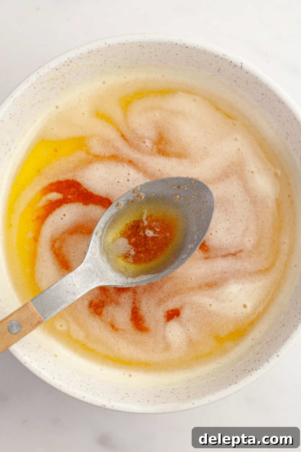 Brown Butter Made Simple 2 A bowl filled with rich, golden brown butter with distinct browned milk solids at the bottom, and a spoon lifting some of the luscious liquid, showcasing its inviting texture and color.