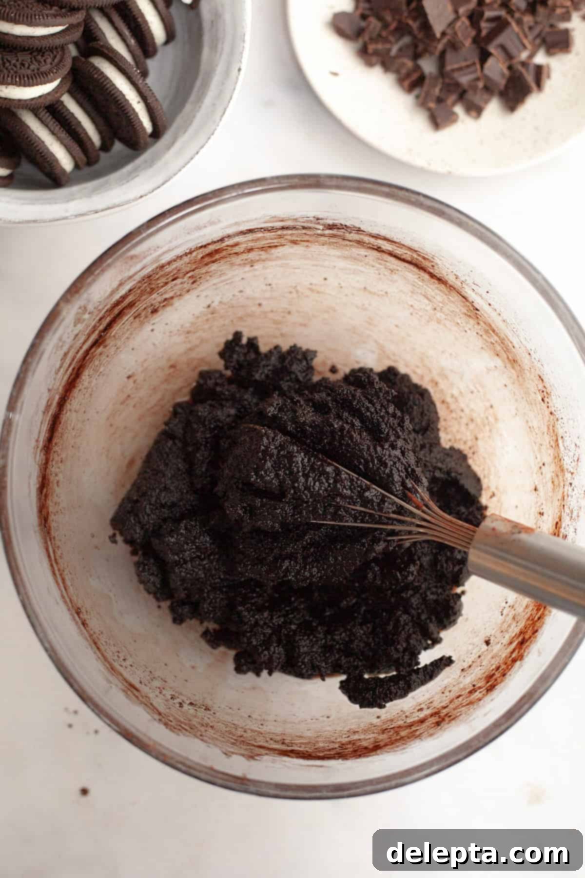 One-Bowl Decadence: Oreo Fudge Brownies 5 A glass bowl containing a grainy mixture of brownie batter with cocoa powders and other ingredients, being whisked.