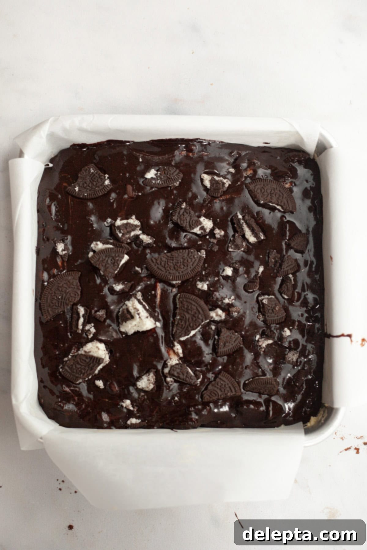 One-Bowl Decadence: Oreo Fudge Brownies 8 Unbaked Oreo brownie batter evenly spread in a parchment-lined square baking pan, topped with extra Oreos.
