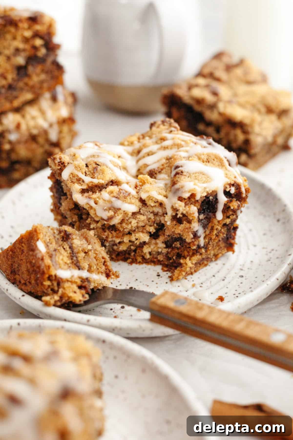 Perfectly Moist Banana Coffee Cake with Tangy Sour Cream 11 Another beautiful slice of banana bread coffee cake, drizzled with white glaze, on a small plate next to a cup of coffee.