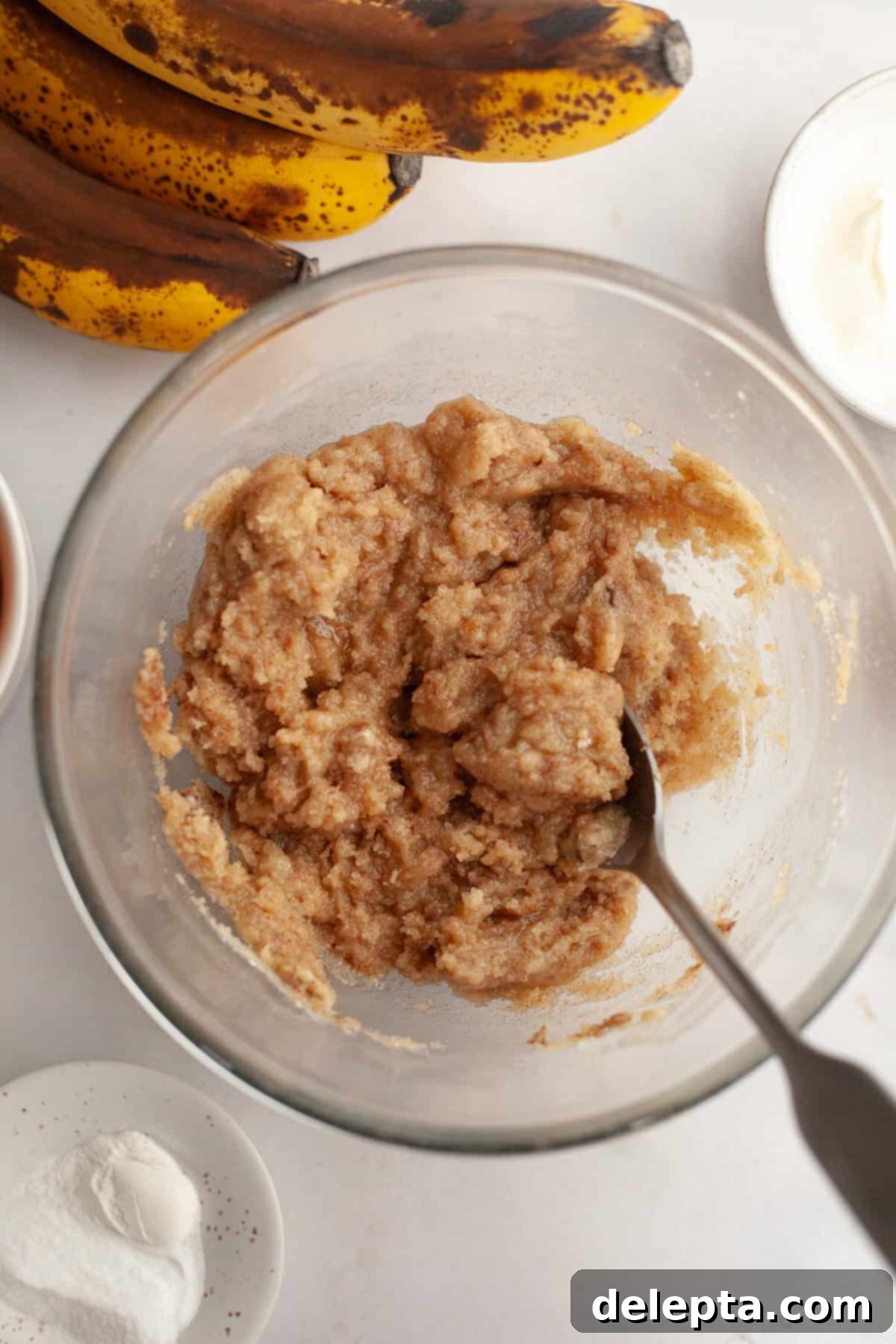 Perfectly Moist Banana Coffee Cake with Tangy Sour Cream 5 A clear glass bowl holding streusel topping with a spoon, ready to be chilled.