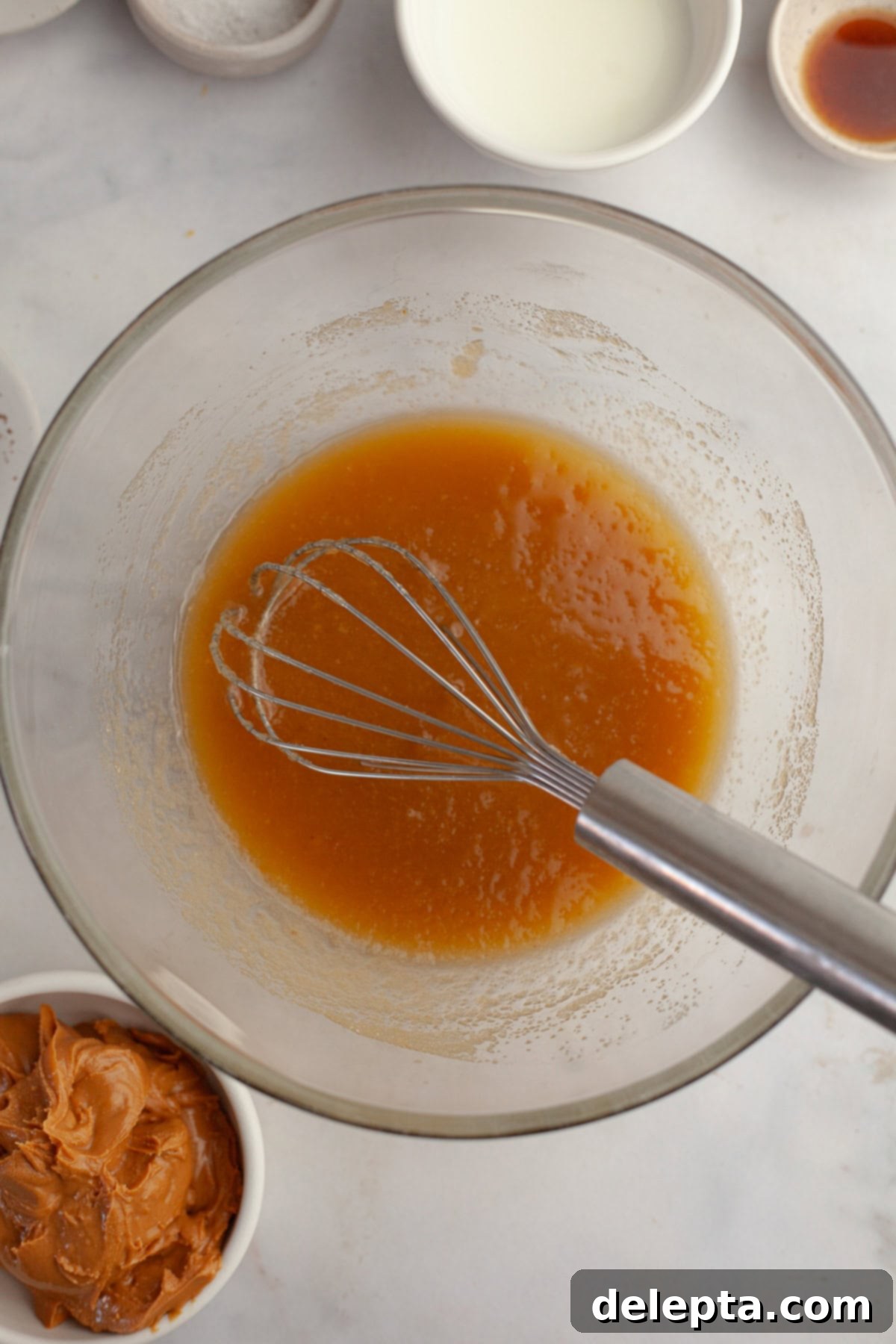 Banana Peanut Butter Bliss 4 A glass bowl with a light brown mixture in it and a whisk, showing the melted butter and sugars combined for the banana cake.