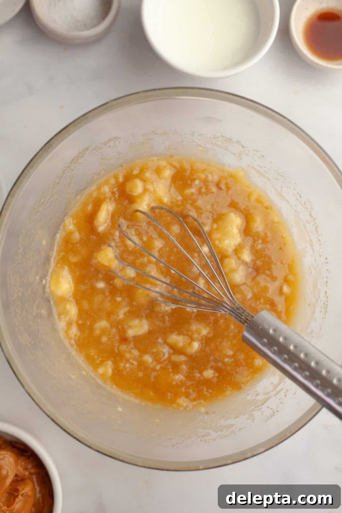 Banana Peanut Butter Bliss 5 Banana cake mixture in a glass bowl with a whisk, showing mashed bananas incorporated into the wet ingredients.