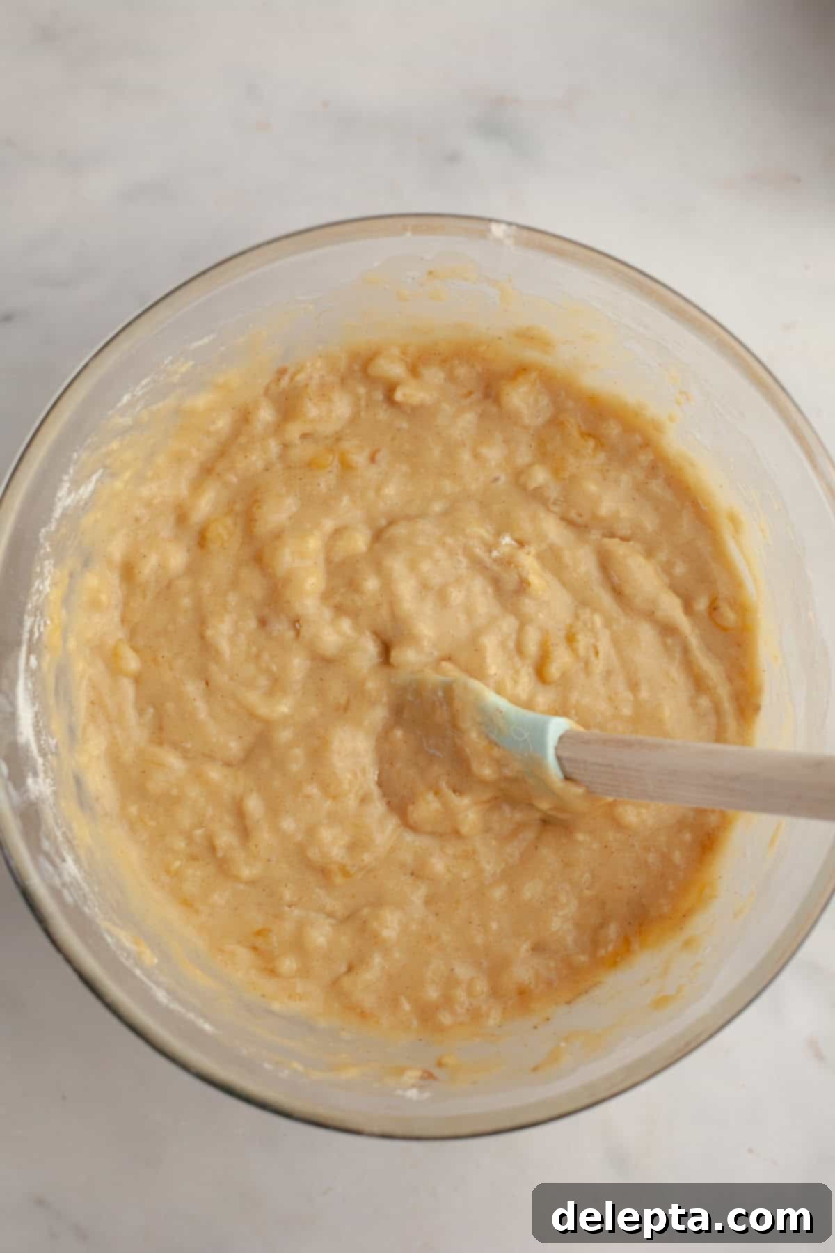 Banana Peanut Butter Bliss 6 Banana cake mixture in a glass bowl with a rubber spatula, demonstrating the gentle folding of dry ingredients.