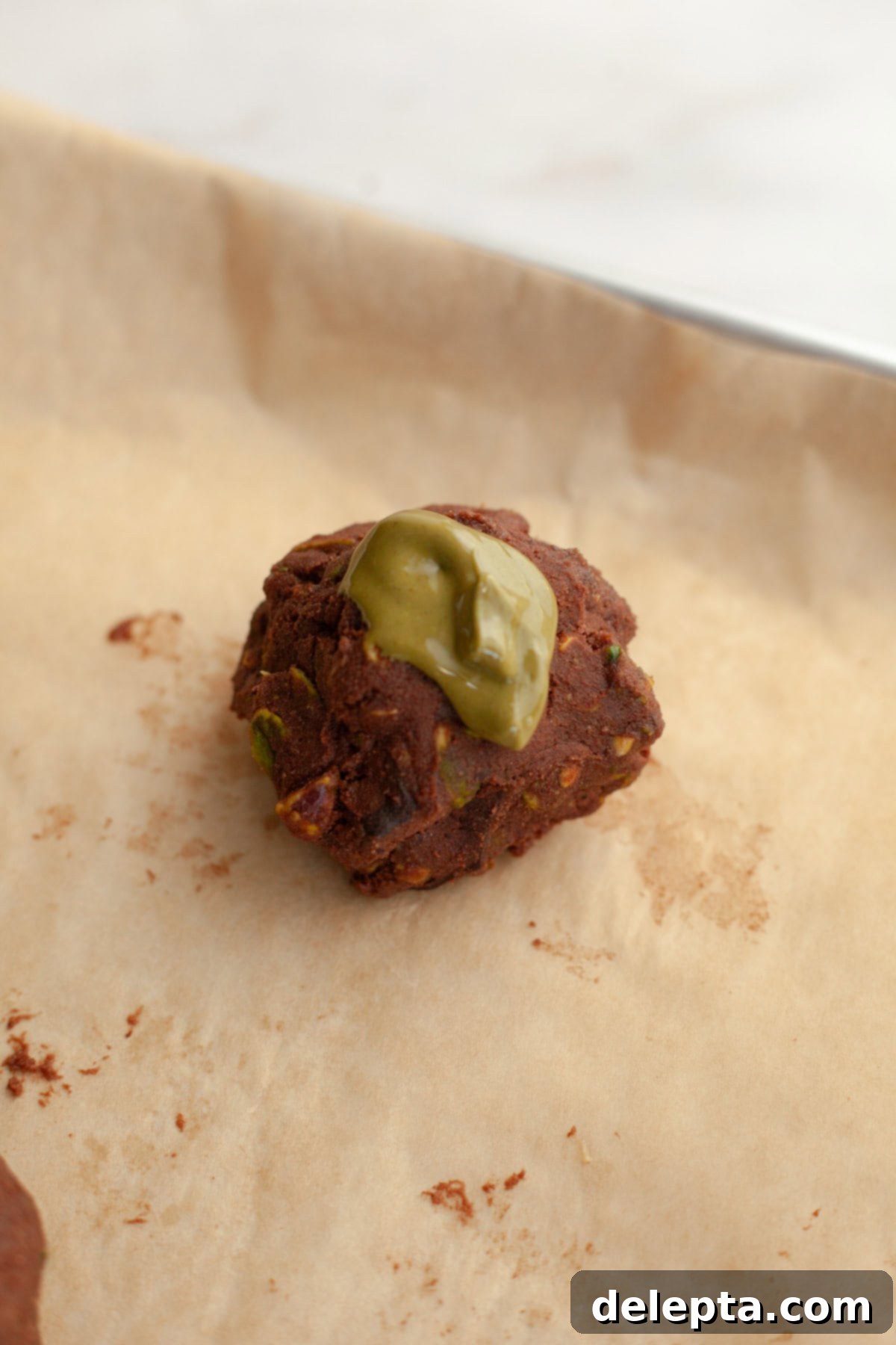 Gooey Pistachio Stuffed One Bowl Chocolate Cookies 11 An unbaked chocolate cookie dough ball, perfectly stuffed, with an optional dollop of pistachio cream on top for a cracked appearance.