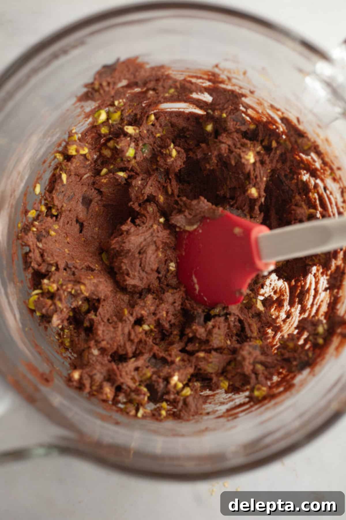 Gooey Pistachio Stuffed One Bowl Chocolate Cookies 8 Chocolate cookie dough in a glass bowl, studded with generous amounts of chopped pistachios and chocolate chunks.