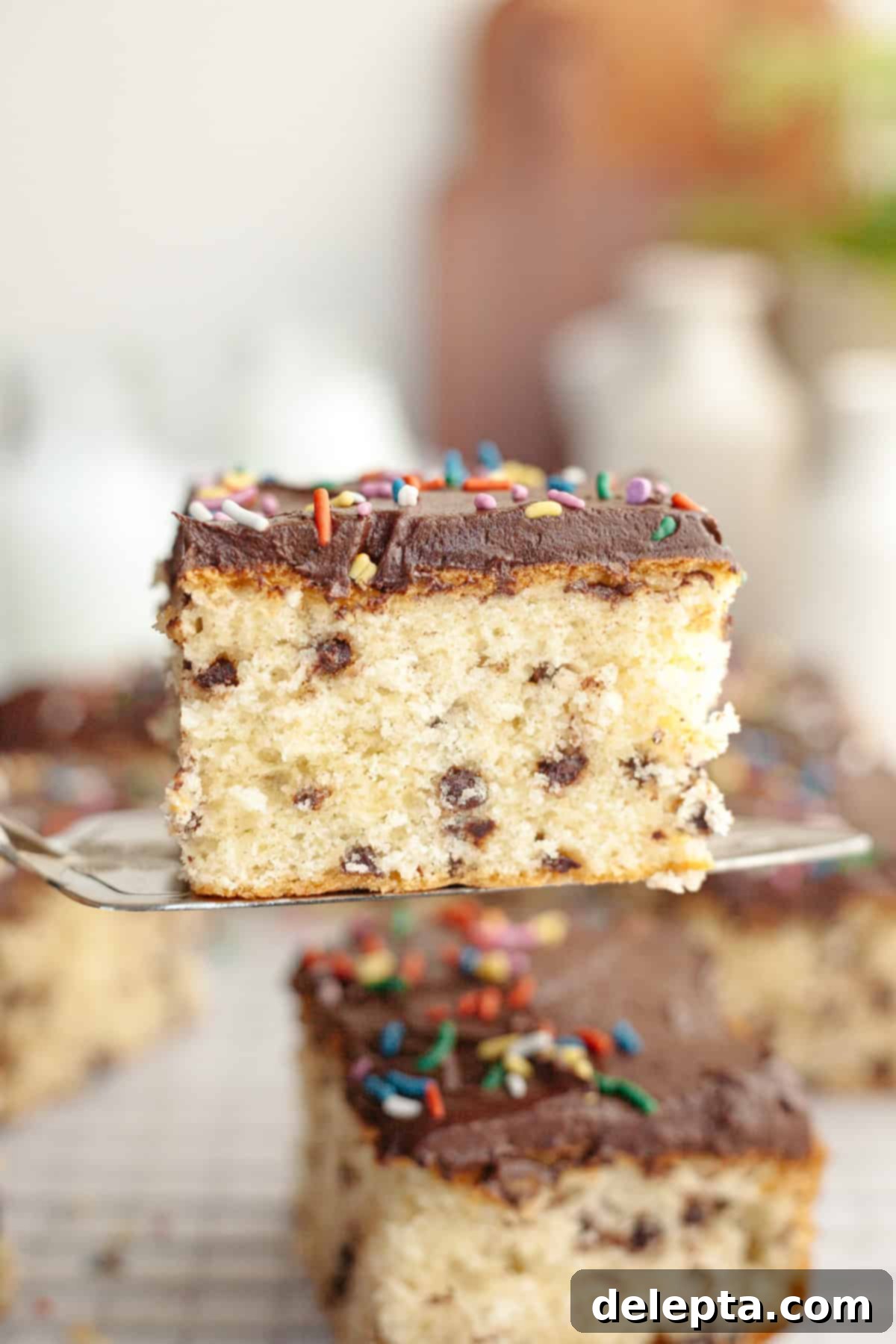 Double Chocolate Chip Sheet Cake 11 A close up of a slice of chocolate chip sheet cake with chocolate frosting on a cake server.