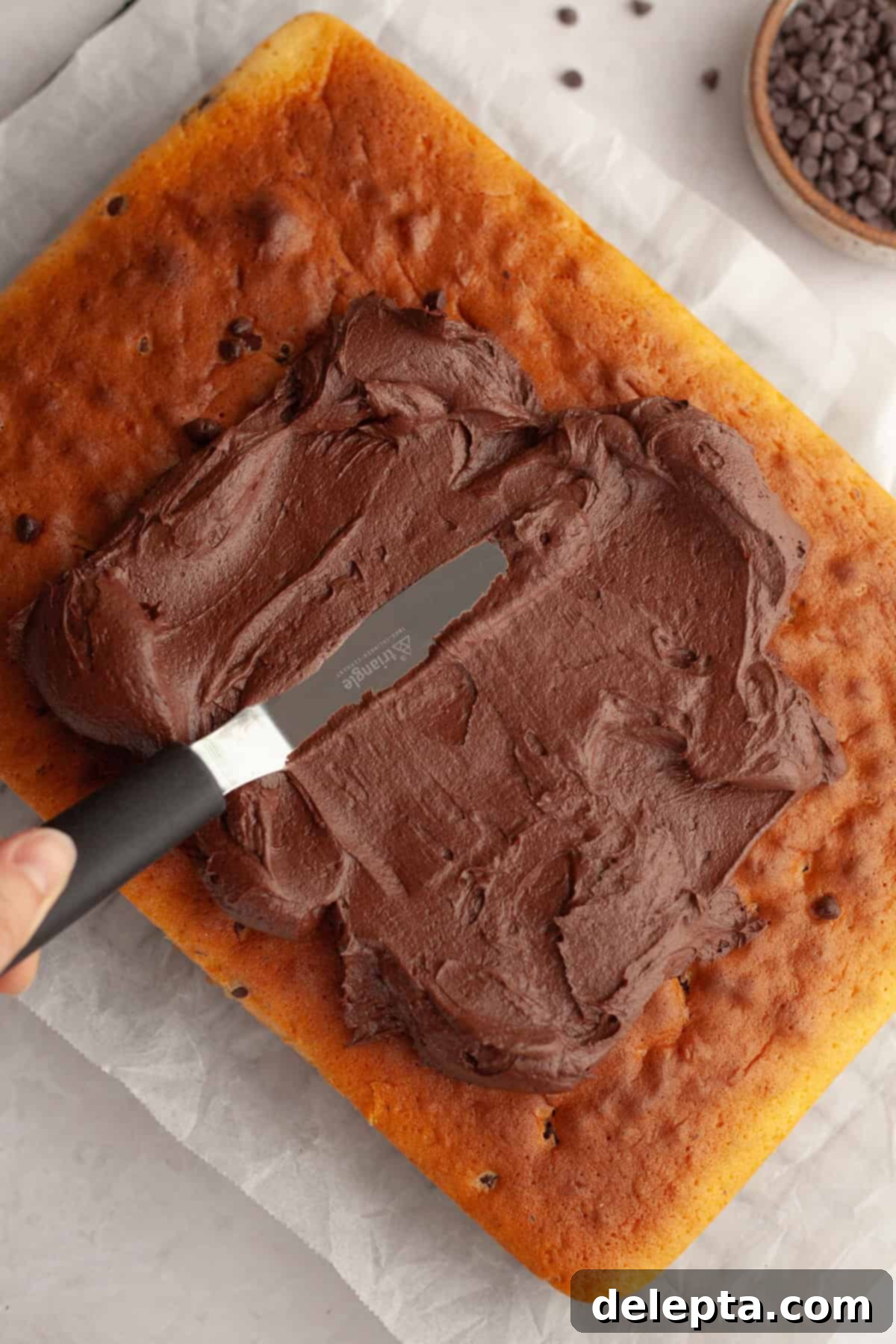 Double Chocolate Chip Sheet Cake 9 Chocolate frosting being spread onto a rectangular sheet cake.