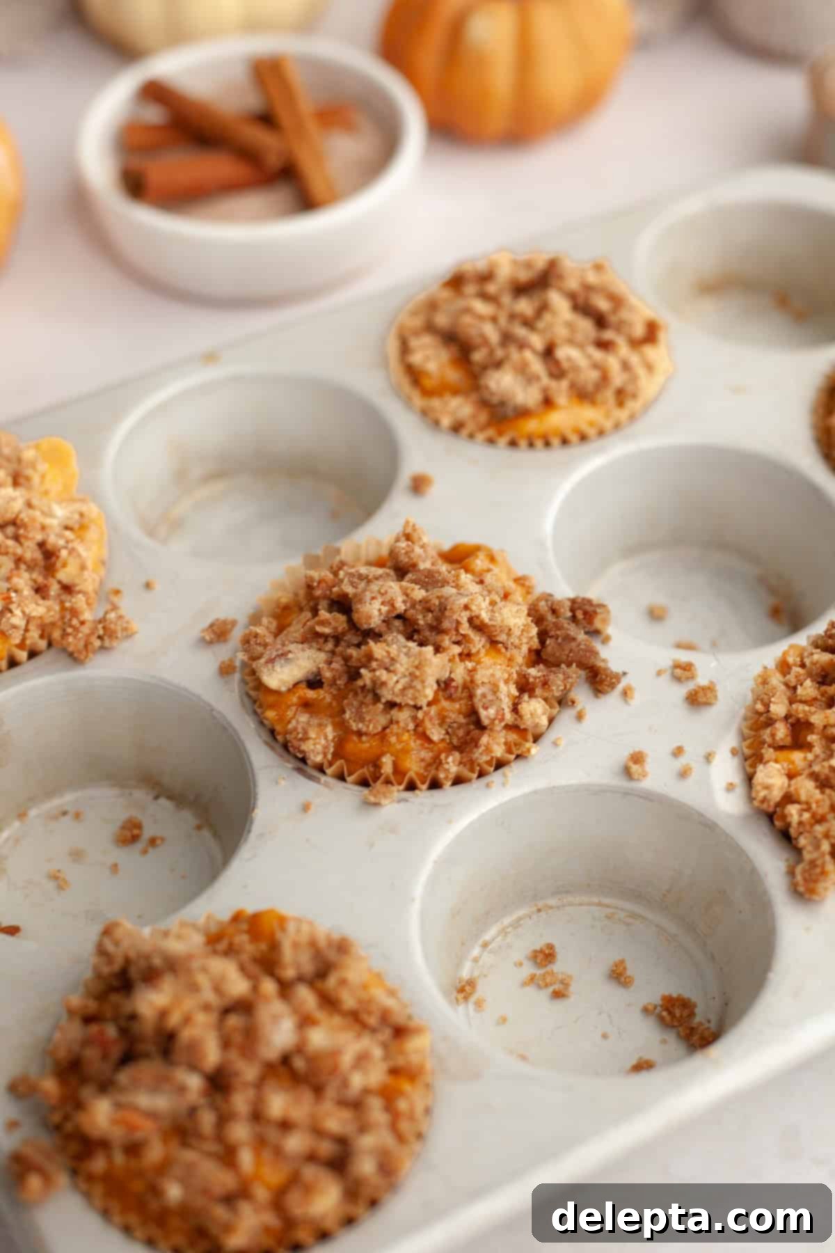 Harvest Pumpkin Pecan Crunch Muffins 7 Unbaked pumpkin muffins, generously topped with pecan streusel, nestled in a muffin pan, ready for the oven.