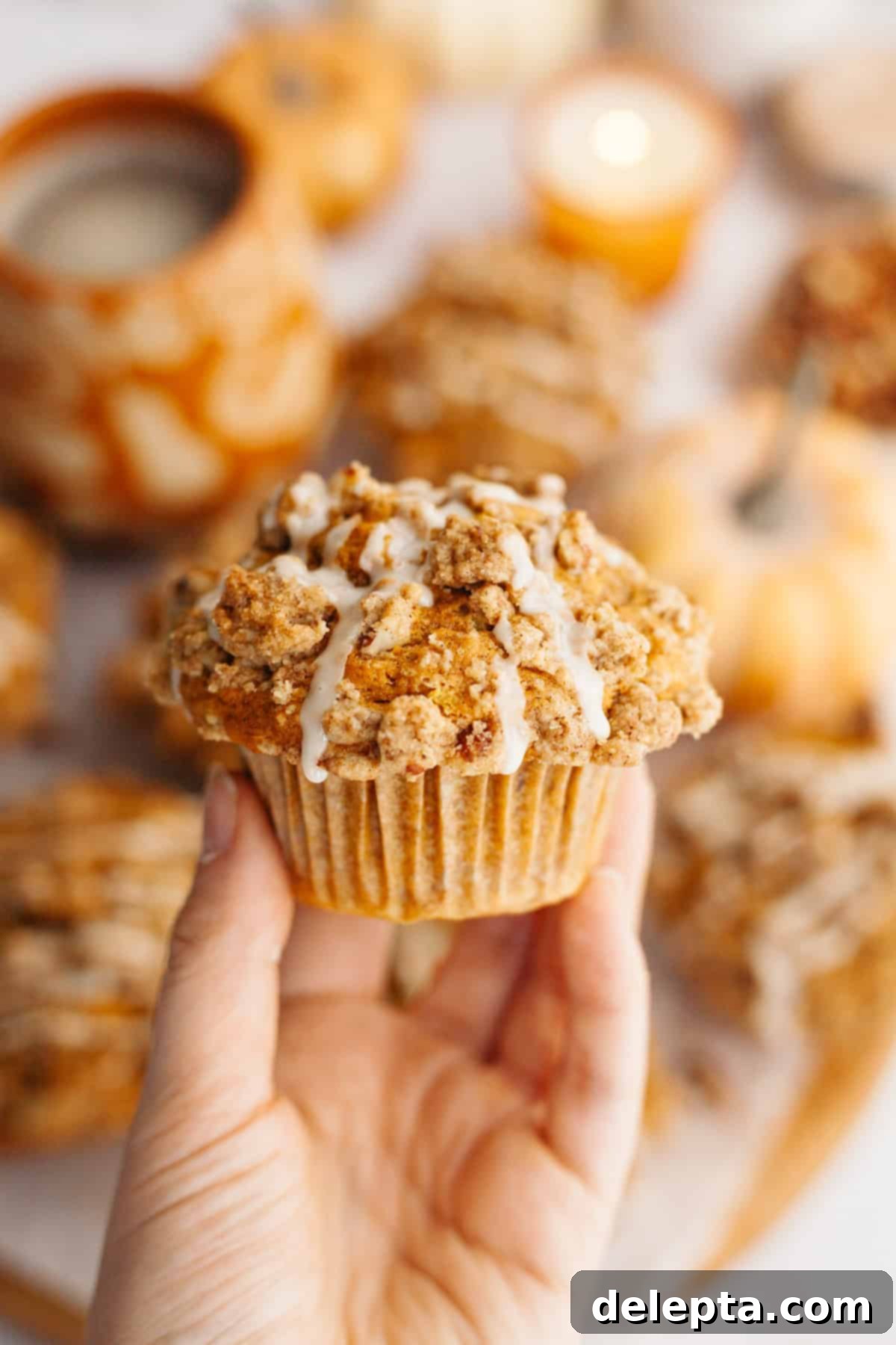 Harvest Pumpkin Pecan Crunch Muffins 8 A hand gently holds a perfectly baked pecan pumpkin muffin, showcasing its golden-brown top and a luscious drizzle of white glaze.