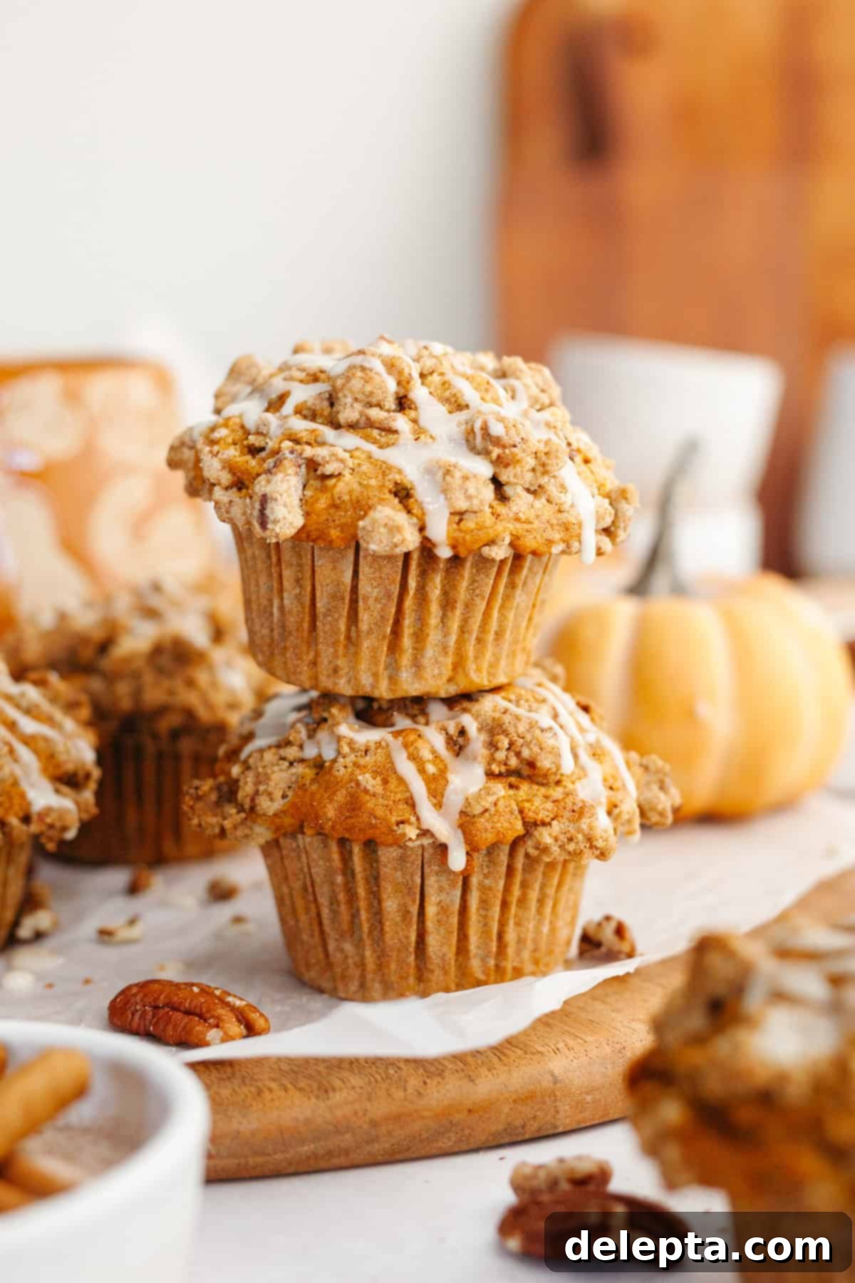 Harvest Pumpkin Pecan Crunch Muffins 9 A charming stack of two pecan pumpkin muffins, each delicately glazed, resting on a rustic wooden board, ready to be enjoyed.