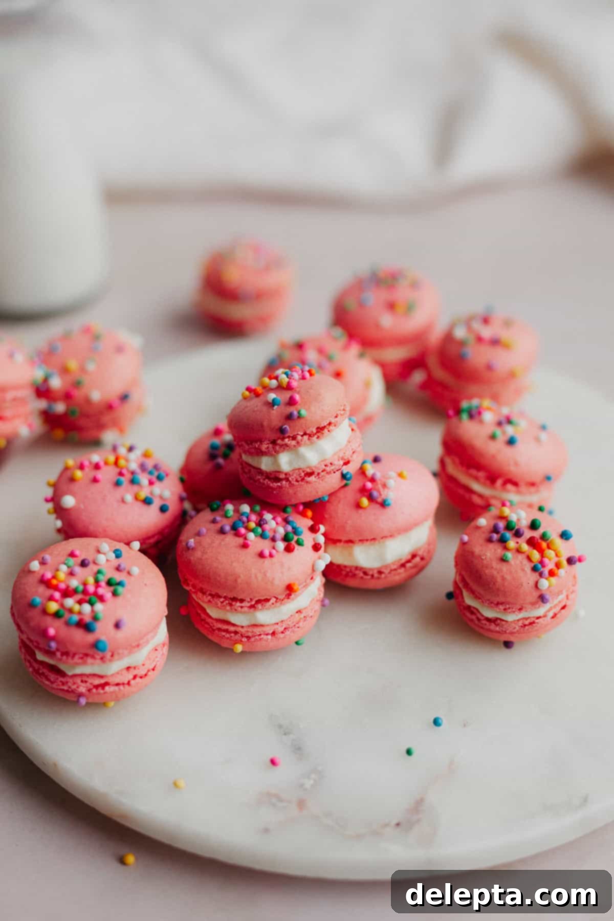 Funfetti Macarons 13 pink sprinkle macarons with a white filling on a circular marble tray.