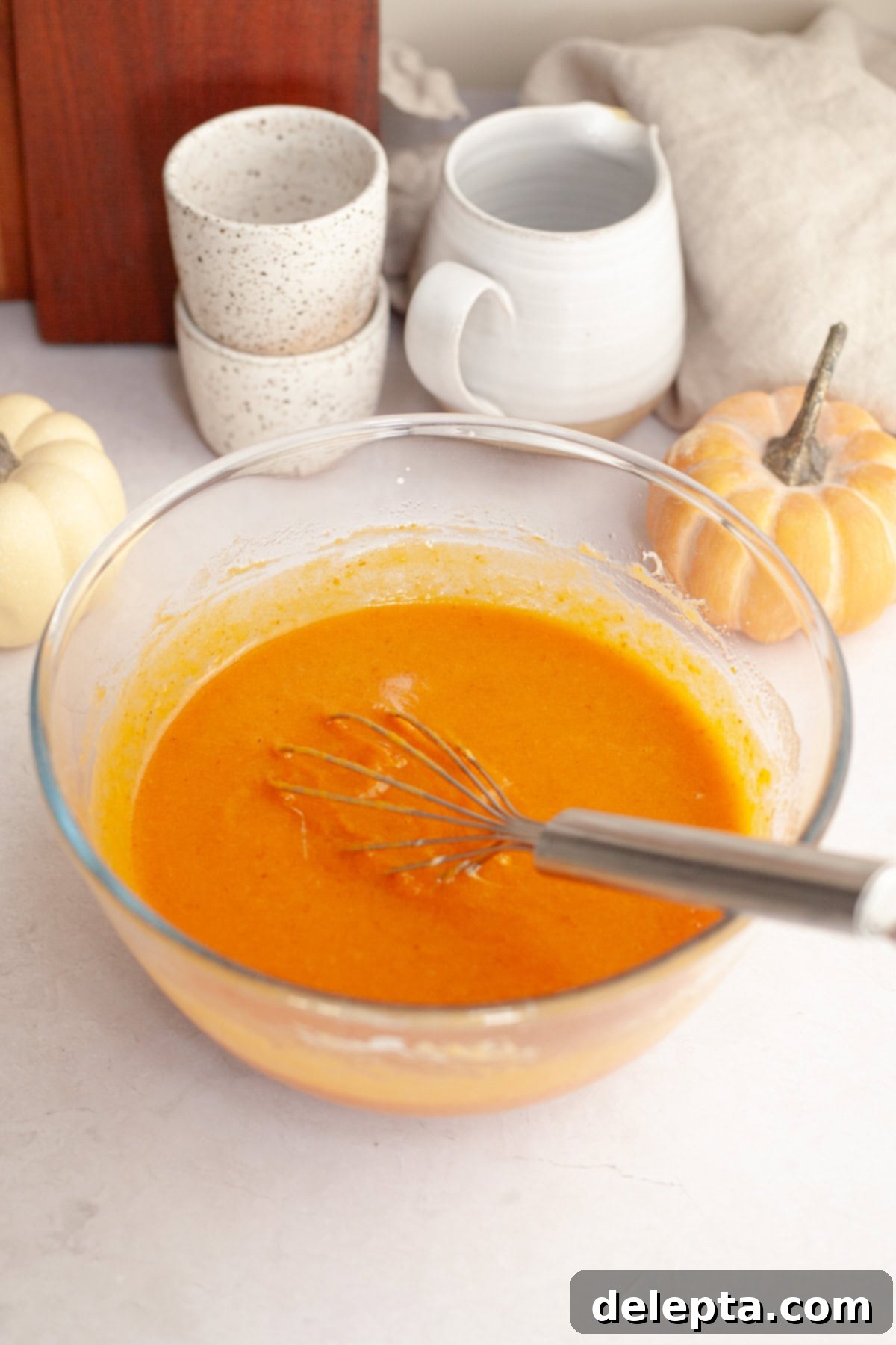 One-Bowl Pumpkin Sour Cream Muffins 4 Smooth pumpkin muffin batter being whisked in a clear glass bowl, showcasing its rich orange color and creamy consistency.
